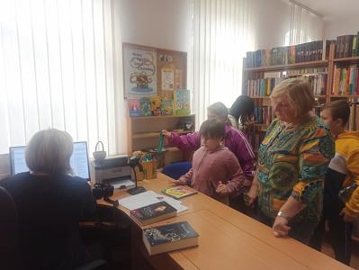 Pani bibliotekarka i uczniowie wypożyczają książki w Miejskiej Bibliotece. 