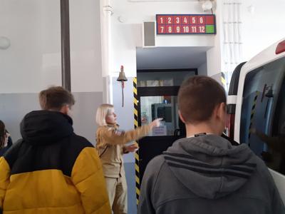 Pani strażak pokazuje uczniom dyspozytornię i tablicę z numerami wozów wyznaczanych do udziału w akcjach