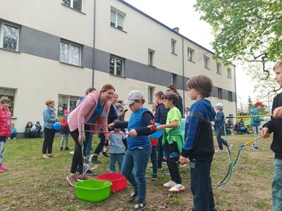 Na zdjęciu uczniowie i nauczyciele biorący udział w zabawach sportowych. Całość odbywała się na zewnątrz budynku.