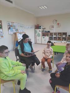 Mama Jasia czyta bajkę. Dzieci z zaciekawieniem słuchają  czytanej książki. 