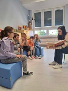 Uczniowie uważnie słuchają jak mama Oli czyta bajkę. 