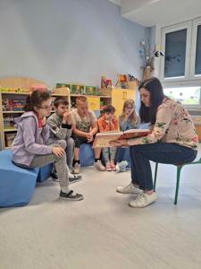 Mama Oli pokazuje dzieciom ilustracje. Dzieci z zainteresowaniem się przygląda