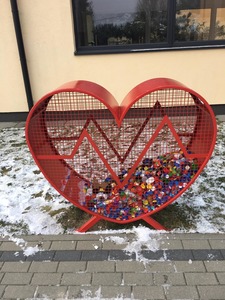 Metalowy pojemnik w kształcie serca z plastikowymi nakrętkami. Jest ustawiony przed naszą szkołą przy chodniku prowadzącym do głównego wejścia.  