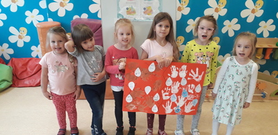 Sześć dziewczynek z przedszkolna stoi na tle kolorowej ściany i trzyma w rękach zrobiony przez nie plakat. 