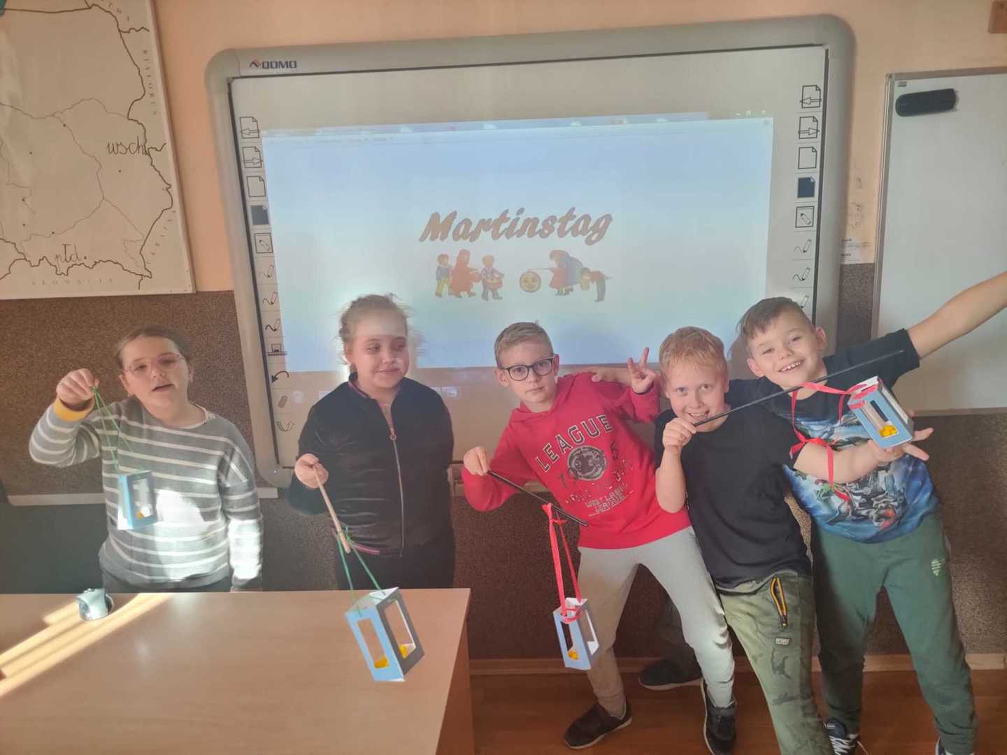 Uczniowie prezentujący własnoręcznie wykonane lampiony. W tle tablica multimedialna.