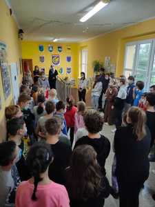 Dzieci stoją na korytarzu, słuchając w skupieniu.