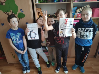  Uczniowie prezentujący efekty swojej pracy - lapbook. W tle szkolne szafy i regały.