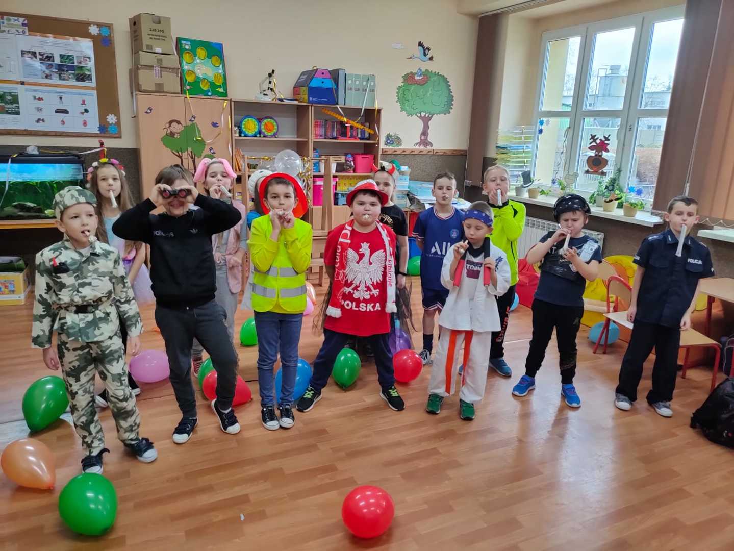 Uczniowie w strojach karnawałowych w udekorowanej sali.