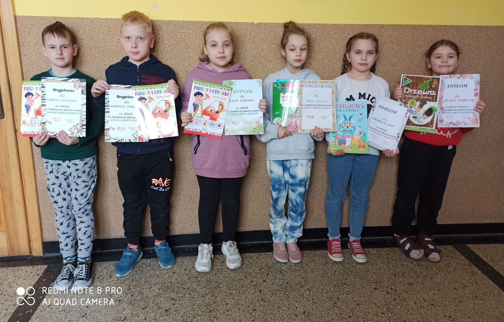 Zdjęcie przedstawia uczniów, którzy trzymają w ręce dyplomy wraz z nagrodami.