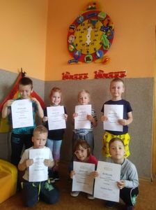Zdjęcie przedstawia uśmiechnięte dzieci z dyplomami, w tle dekoracja znajdująca się w sali lekcyjnej.