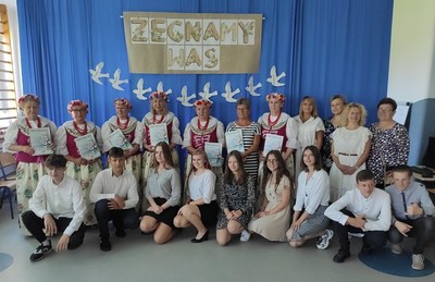 W pierwszym rzędzie uczniowie klasy VIII. W drugim rzędzie Dyrektor Szkoły Pani Mariola Kuliś, Wiceburmistrz Pani Beata Bacior,  Wychowawczyni klasy VIII Pani Dominika Cieślak, Panie z Koła Gospodyń Wiejskich z Ligoty Woźnickiej. W tle dekoracja na zakończenie Roku Szkolnego z napisem "Żegnamy Was".