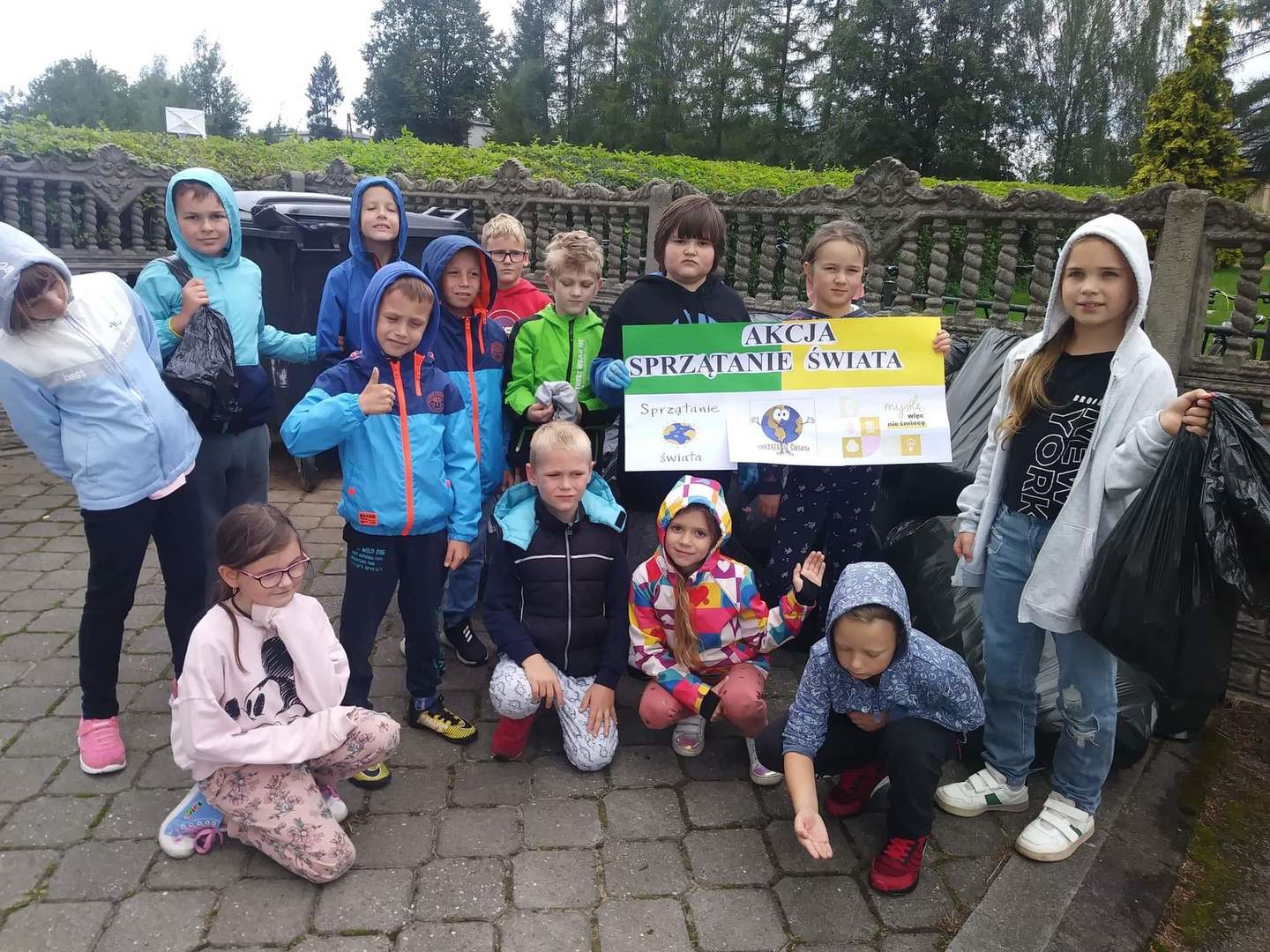 Zdjęcie przedstawia uczniów klas I i III, którzy wzięli udział w akcji „Sprzątanie świata”, chłopiec oraz dziewczynka trzymają plakat „Akcja sprzątanie świata”, w tle boisko szkolne.