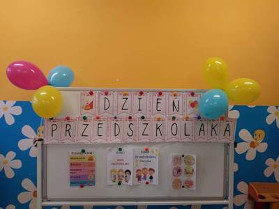 Zdjęcie przedstawia tablicę dekoracyjną z napisem „Dzień Przedszkolaka”, kolorowe balony.
