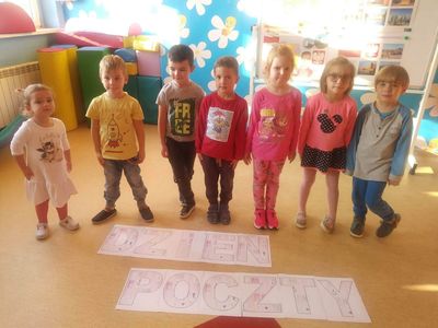 Zdjęcie przedstawia przedszkolaków z napisem Dzień Poczty, w tle sala przedszkolna.