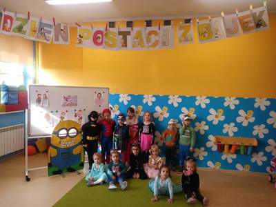 Zdjęcie przedstawia grupę przedszkolaków w strojach bohaterów z bajek, w tle napis „Dzień postaci z
bajek”, sala przedszkolna.