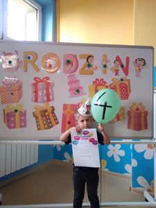 Zdjęcie przedstawia uśmiechniętego Tymona z dyplomem, balonikiem, w tle dekoracja.