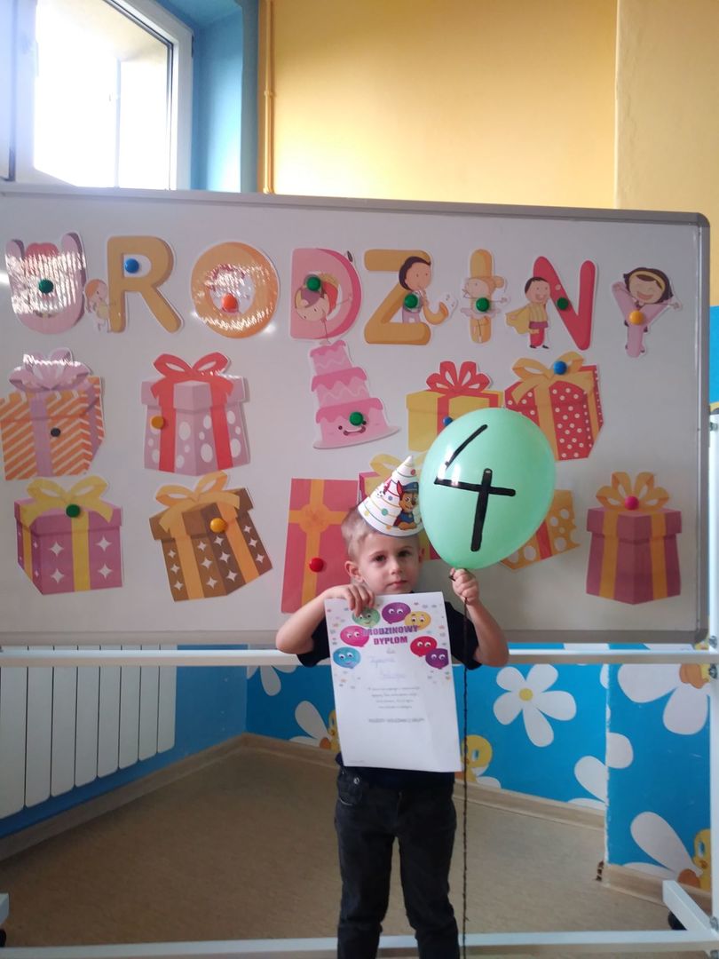 Zdjęcie przedstawia uśmiechniętego Tymona z dyplomem, balonikiem, w tle dekoracja.