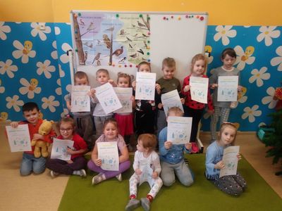 Zdjęcie przedstawia uśmiechniętą grupę przedszkolaków z dyplomami, w tle sala przedszkolna.