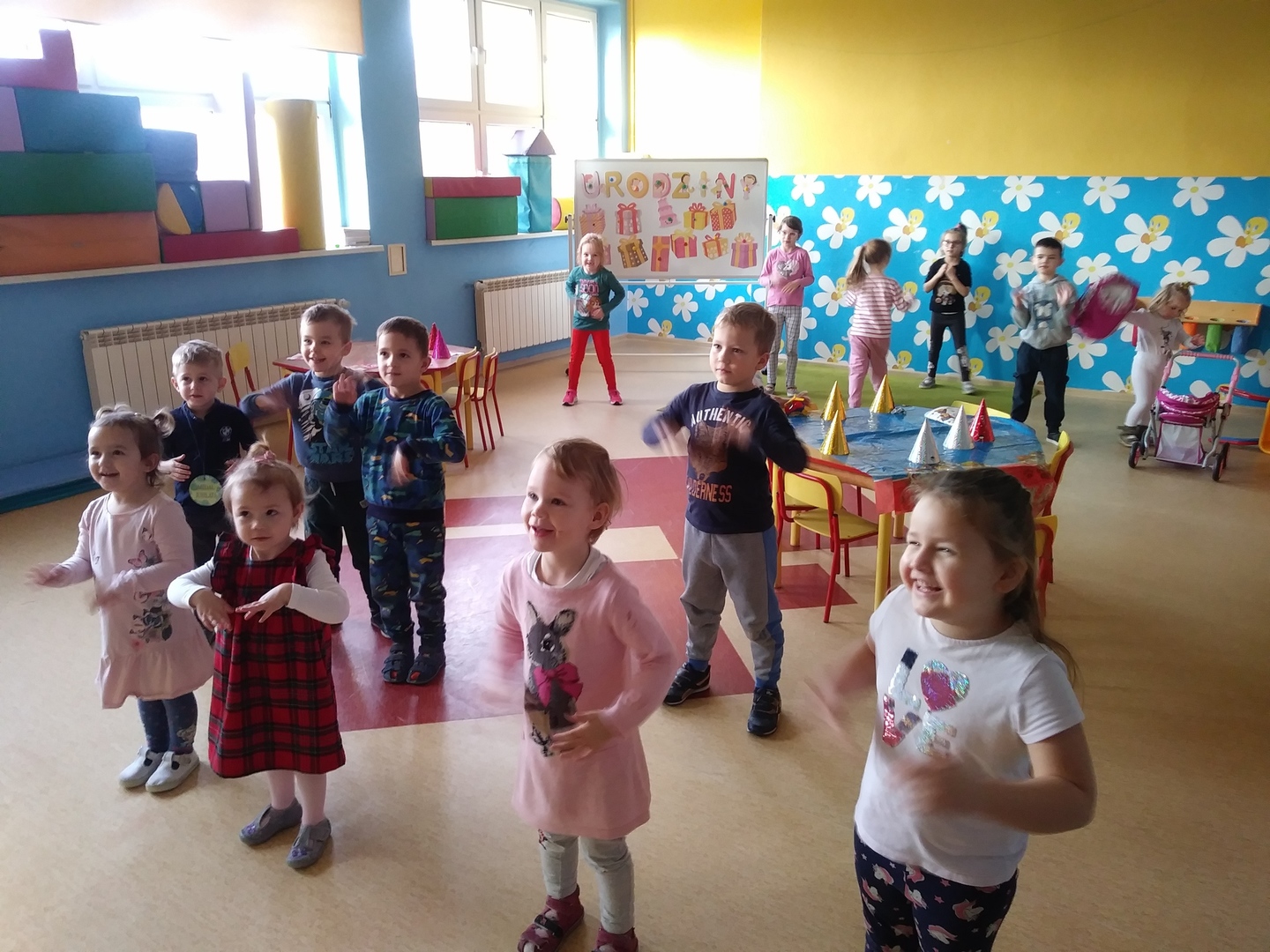 Zdjęcie przedstawia uśmiechniętą grupę przedszkolną podczas gimnastyki i tańców.