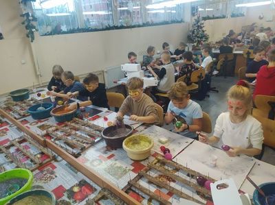 uczniowie siedzący w hali przy długich stołach, w czasie pracy nad ozdabianiem bombek