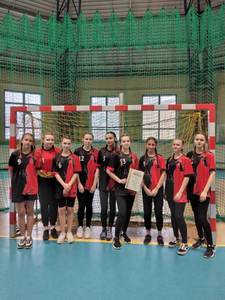 drużyna dziewcząt w czerwono - czarnych koszulkach, na tle bramki