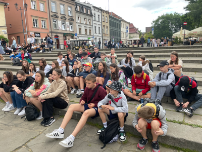 Uczniowie słuchają przewodnika, siedzą na schodach