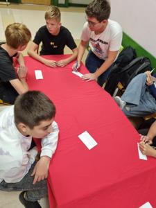 uczniowie siedzą przy stole i wypełniają karty do głosowania