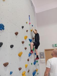 Chłopiec na ściance wspinaczkowej, próbuje sięgnąć trąbkę.