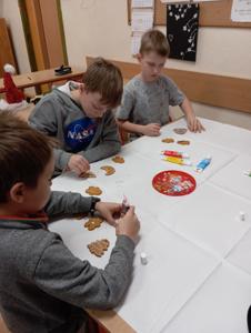 Chłopcy siedzą przy stolikach i malują ciasteczka pisakami spożywczymi.