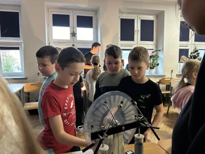 Chłopcy z klasy 2a obserwują przepływ ładunku elektrycznego z wykorzystaniem maszyny elektrycznej.