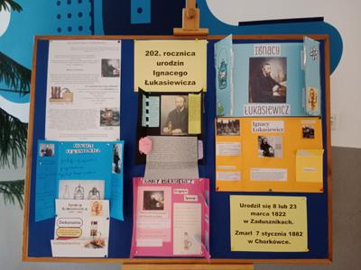Gazetka na szkolnym korytarzu, na której przywieszone są prace uczniów klas 8 przedstawiające postać Ignacego Łukasiewicza.