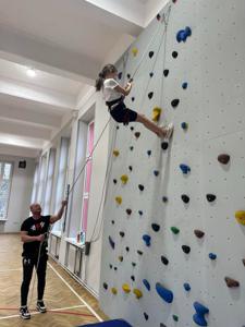 Dziewczynka w uprzęży przy asekuracji instruktora schodzi ze ścianki.