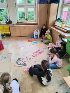 uczniowie siedzą na dywanie i prezentują swoją pracę