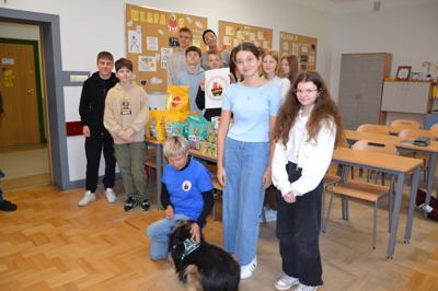 Podopieczny fundacji LAMPO z opiekunką, a w tle wolontariusze z klasy 8c przy darach dla schroniska
