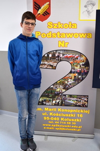 uczeń stoi przy banerze szkoły