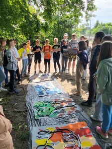 Grupa uczniów stoi wokół prac plastycznych rozłożonych na ziemi 