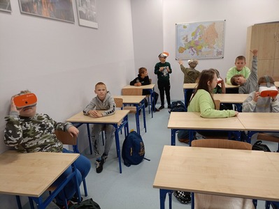 Uczniowie siedzą w ławkach, mają na sobie okulary 3D