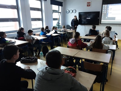 uczniowie klasy 5 siedzą w sali lekcyjnej i słuchają osób prowadzących zajęcia