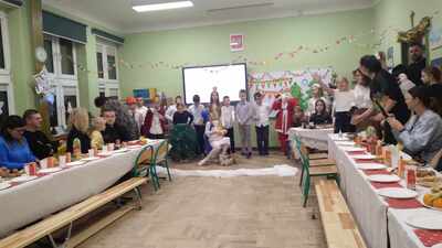 rodzice uczniów, siedzący za stołami w sali lekcyjnej, oglądają występy dzieci