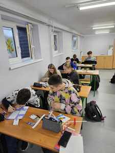 Uczniowie w ławkach lekcyjnych wykonują prace plastyczne