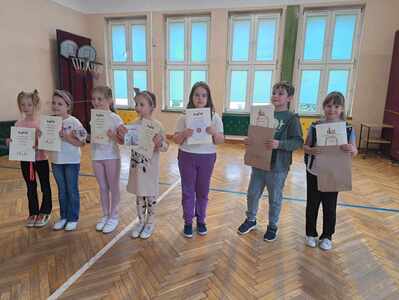 Siedmioro nagrodzonych uczniów stoi w auli szkolnej trzymając dyplomy 