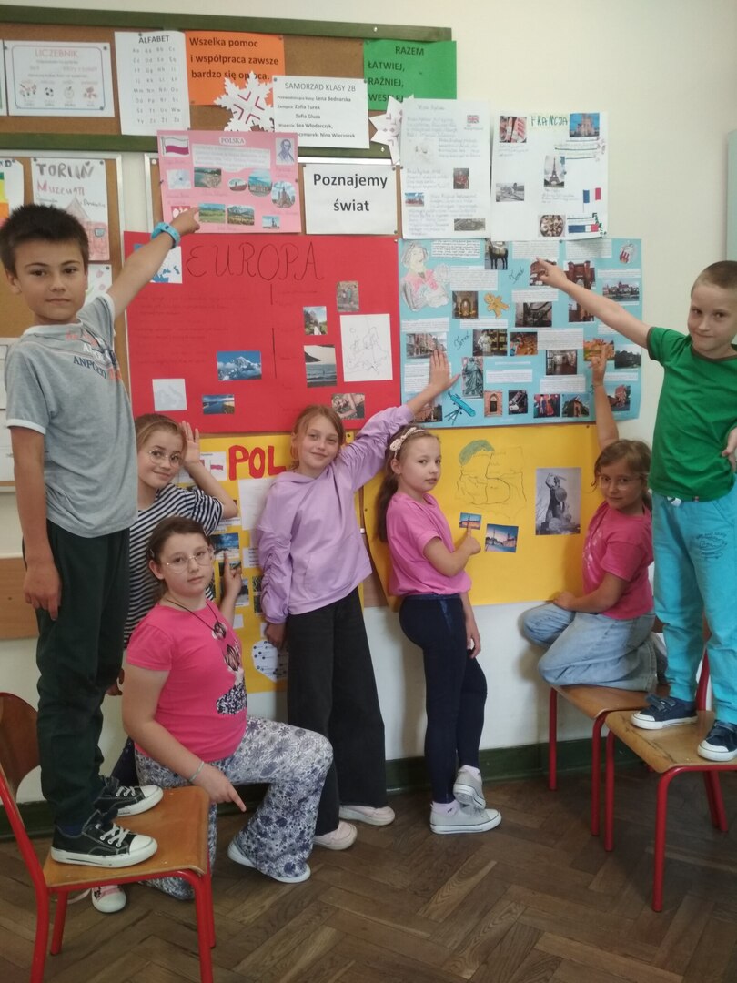 Uczniowie przy tablicy korkowej prezentują plakaty o Europie i miastach europejskich.