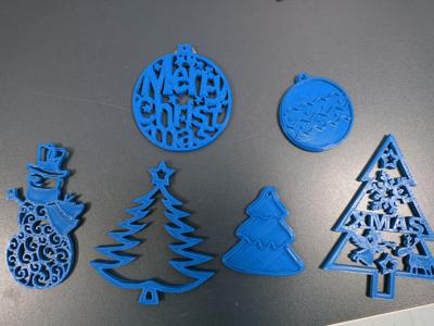 Ozdoby świąteczne wydrukowane na drukarce 3d: bałwan, ozdoby w kształcie choinek, ozdoba z napisem Merry Christmas.
