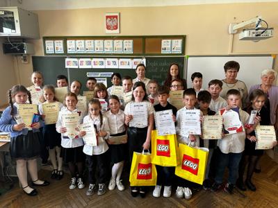 dzieci w strojach szkolnych stoją z dyplomami i nagrodami w rękach, za nimi kilka nauczycielek