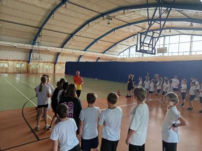 Uczniowie klas czwartych w strojach sportowych stoją w hali sportowej