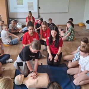 Uczniowie siedzą wokół fantomu i obserwują pokaz masażu serca