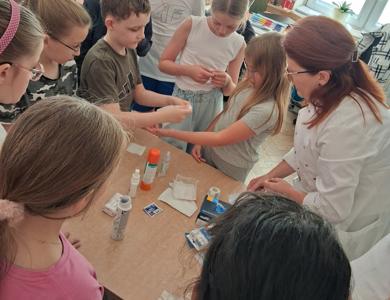Chłopiec pod kierunkiem pielęgniarki zakłada koleżance opatrunek.