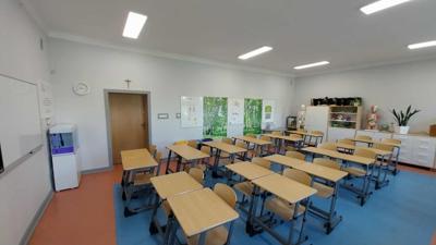Widok sali lekcyjnej z ławkami, meblami i akwarium.