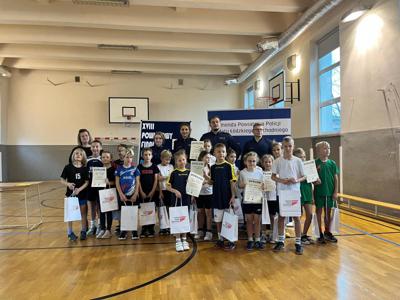 Grupa 20 dzieci klas drugich stoi w sali gimnastycznej w towarzystwie 4 funkcjonariuszy Policji