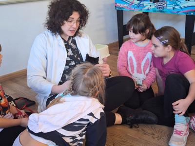 Uczniowie siedzą na podłodze przed lekarką weterynarii, przyglądają się kotu.